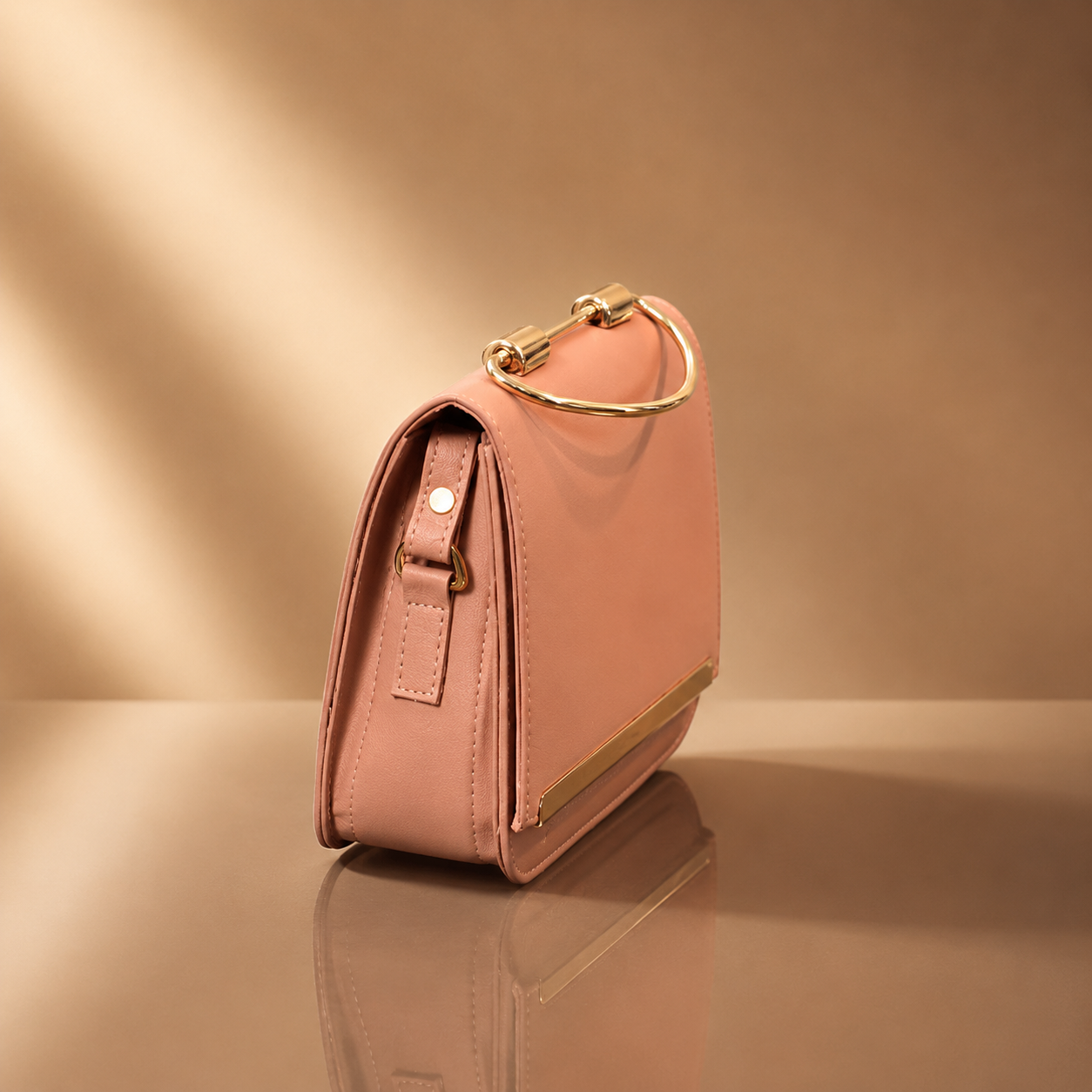 Pink handbag with gold accents on a reflective surface and beige background