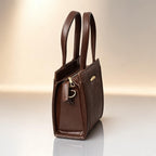 Brown leather handbag with gold accents on a reflective surface and light background