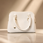White handbag with gold accents on a reflective surface and beige background
